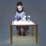 Kind speelt met lichtdoorlatende materialen op de houten Tickit lichttafel